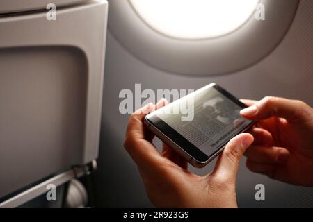 Hands of woman holding smart phone with news article on display in airplane Stock Photo
