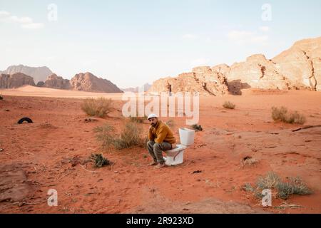 Thoughtful man sitting on toilet seat and defecating in desert Stock Photo