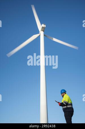 Engineer using tablet PC standing near wind turbine Stock Photo