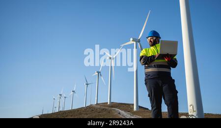 Engineer working on laptop standing at wind park Stock Photo