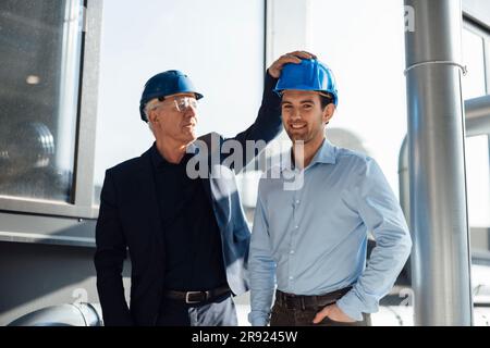 Happy engineers wearing hardhats standing at industry Stock Photo