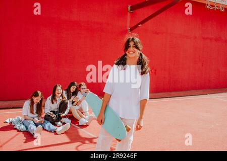 Teenage girl with friends spending leisure time in front of red wall at playground Stock Photo