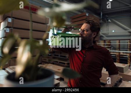 Thoughtful mature businessman standing with toolbox in factory Stock Photo