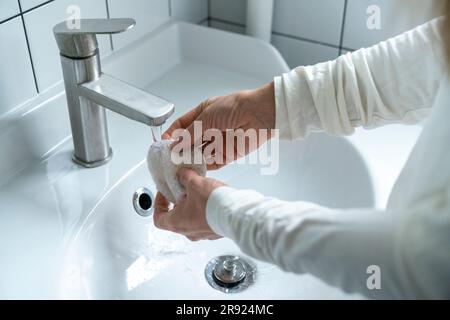 Hands of woman washing bath sponge in bathroom sink Stock Photo