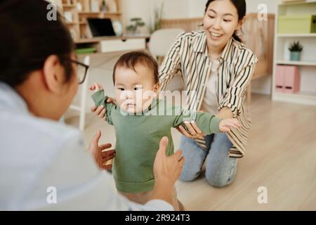 Father and mother supporting daughter taking first steps at home Stock Photo