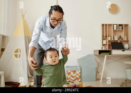 Father supporting daughter taking first steps at home Stock Photo