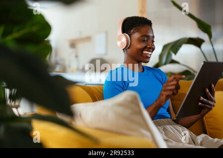 Happy young freelancer using tablet PC on sofa Stock Photo