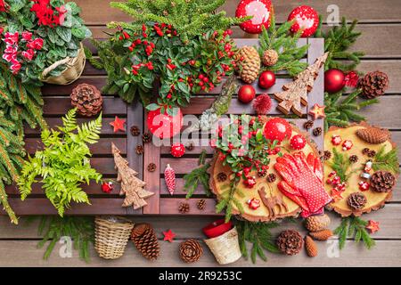 Winter plants, pine cones, Christmas decorations, wooden coasters and gardening gloves on table Stock Photo