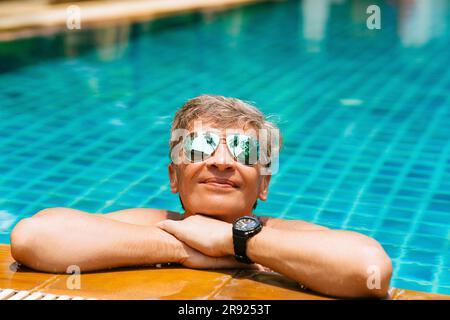 Smiling man wearing sunglasses relaxing in swimming pool Stock Photo