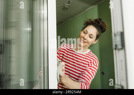 Smiling woman cleaning window frame Stock Photo