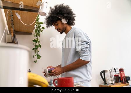 Man wearing headphones doing dishes in kitchen at home Stock Photo