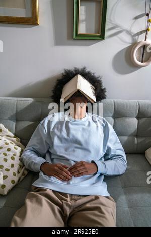 Tired man sleeping on sofa with book on face at home Stock Photo