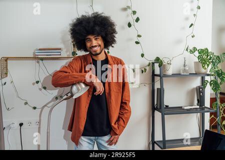 Smiling man leaning on desk lamp at home Stock Photo