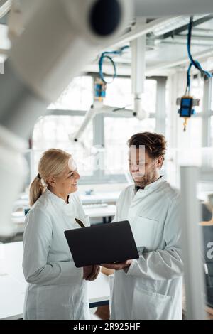 Happy senior scientist discussing with colleague using laptop at laboratory Stock Photo
