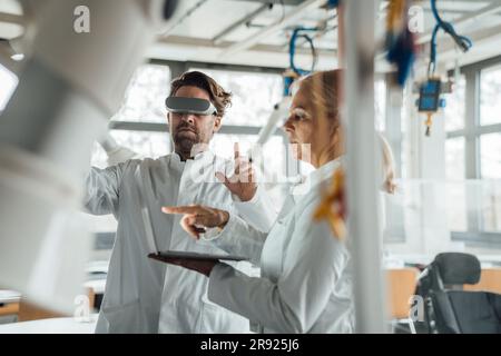 Senior scientist using laptop with colleague wearing virtual reality simulator in laboratory Stock Photo