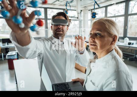 Scientist wearing virtual reality simulator examining molecular structure with colleague Stock Photo