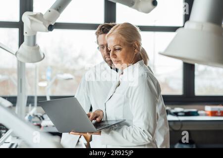 Mature scientist with colleague using laptop Stock Photo