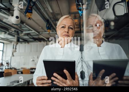 Thoughtful scientist with tablet PC standing by glass cabinet Stock Photo