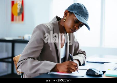 Freelancer wearing cap taking down notes at office Stock Photo