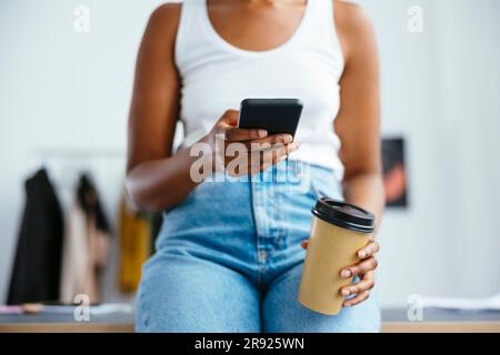 Freelancer using smart phone holding disposable coffee cup Stock Photo