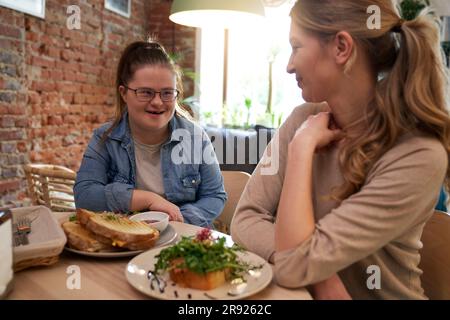 Happy woman with down syndrome having breakfast with friend in cafe Stock Photo