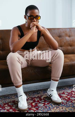 Young woman with hands clasped sitting on sofa Stock Photo