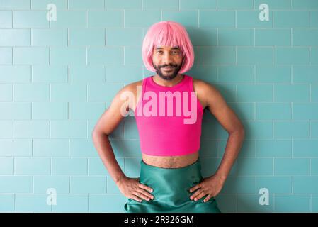 Young queer man standing with arms akimbo in front of tiled wall Stock Photo