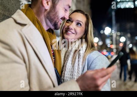 Happy young woman with man holding smart phone Stock Photo