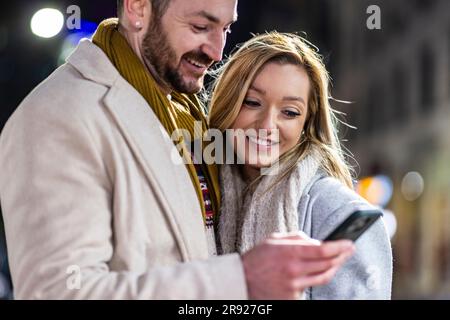 Smiling man and woman using mobile phone together Stock Photo