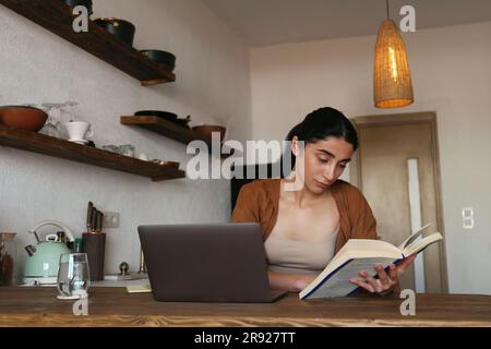 Woman studying with book and laptop on table at home Stock Photo