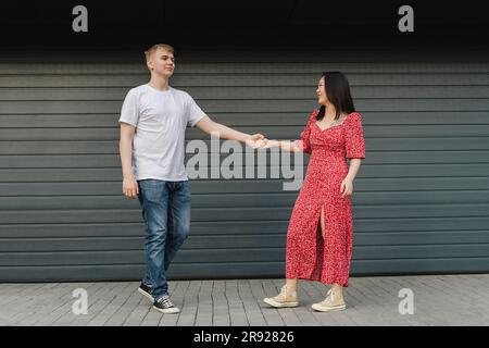 Romantic young couple holding hands in front of closed shutter Stock Photo