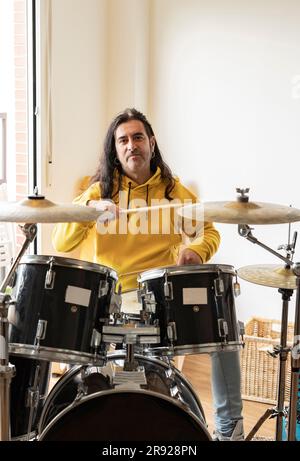 Smiling mature musician playing drum at home Stock Photo