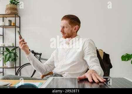 Businessman sitting with solar panel and using smart phone at desk Stock Photo