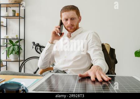 Businessman touching solar panel and talking on smart phone in office Stock Photo