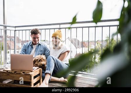 Happy young couple sitting with dog and using laptop Stock Photo