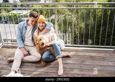 Loving young couple sitting with dog on balcony Stock Photo