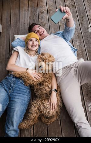 Happy young couple taking selfie with dog and lying on floor Stock Photo