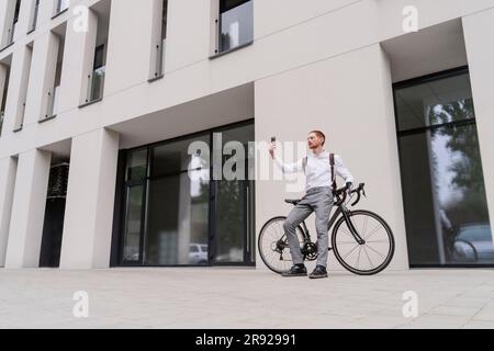 Businessman with bicycle video calling on smart phone Stock Photo
