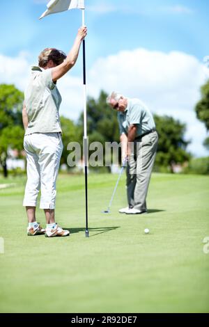 Woman with flag, old man or golfer on golf course for a birdie, putting stroke or exercise in retirement. Senior couple, mature or serious player Stock Photo