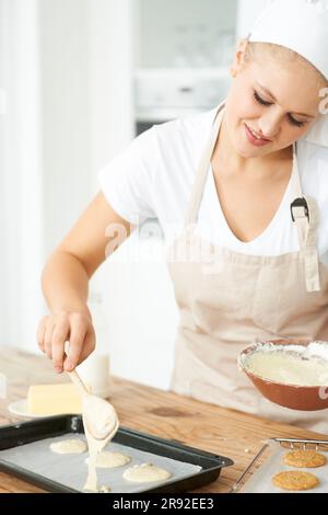 Happy woman, tray or chef baking cookies with dough or pastry in a bakery kitchen with recipe. Food business, dessert or girl baker smiling or working Stock Photo