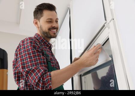 Worker in uniform installing roller window blind indoors Stock Photo