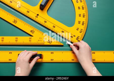 Woman drawing with chalk, ruler, triangle and protractor on green board, closeup Stock Photo