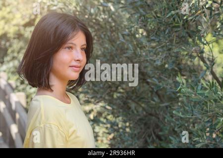 Portrait of a cute girl on a background of greenery in sunny weather. Stock Photo