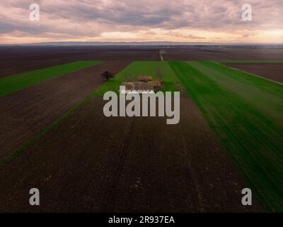 Aerial flight over Winter Agricultural fields with abandoned ranch during Sunset. Vojvodina, Serbia, Europe. Stock Photo