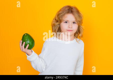 Kid hold red avocado in studio. Studio portrait of cute child with avocado isolated on yellow background Stock Photo