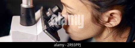 Asian lady doctor looks into contemporary microscope researching sample on slide in hospital Stock Photo