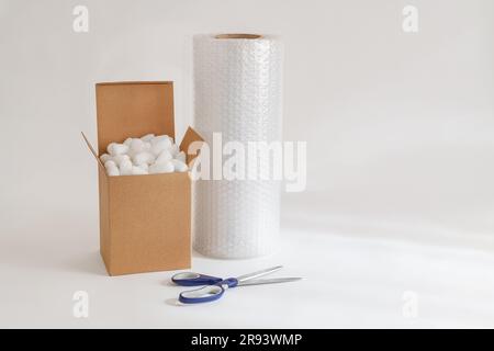 Cardboard box isolated on the white background filled with packing peanuts, bubble wrap and scissors Stock Photo