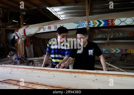 (230624) -- FUZHOU, June 24, 2023 (Xinhua) -- Fang Shaohuang (L), an inheritor of the city-level intangible cultural heritage of dragon boat making techniques, talks with his nephew Fang Jianwei at a dragon boat factory in Minhou of southeast China's Fujian Province, on May 30, 2022. The Dragon Boat Festival, also known as Duanwu Festival, traditionally falls on the fifth day of the fifth month in the Chinese lunar calendar. The dragon boat competition, a traditional part of the festival, has gained popularity on both sides of the Taiwan Strait, bringing excitement to a wide range of people. Stock Photo