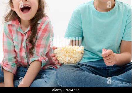 Details on a bowl of popcorn in the hands of cute children watching movies or cartoons over white isolated background Stock Photo