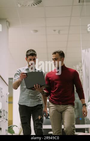 Two creative young business people walking at the office and discussing. They are carrying a lap top. Low angle view photo Stock Photo